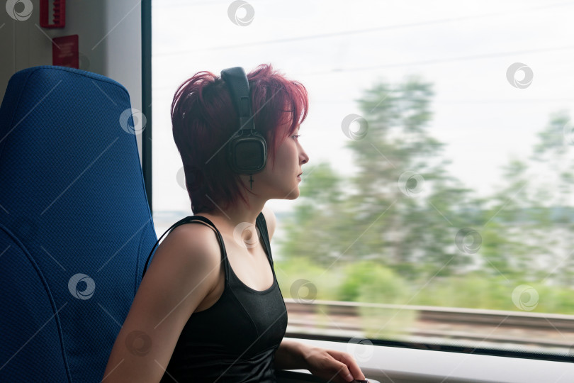 Скачать молодая женщина едет в пригородном поезде и смотрит в окно на пейзаж за окном, размытый в движении фотосток Ozero