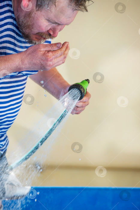 Скачать мужчина пьет воду из шланга в жаркий день. фотосток Ozero