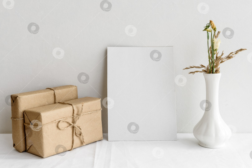 Скачать Пустая белая поздравительная открытка, подарочные коробки ручной работы и засушенные цветы в вазе на белом фоне. Романтический фон для приглашения. фотосток Ozero