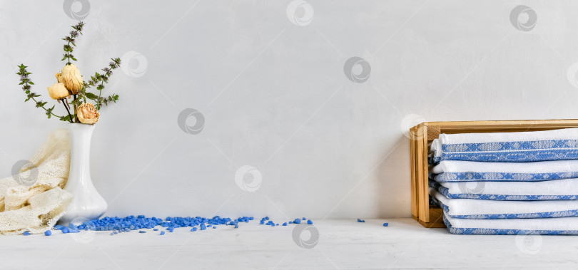Скачать модный фон гигиенических принадлежностей - льняные полотенца, сложенные в деревянную коробку, и засушенные цветы в вазе на белом столе. Уютный домашний фон. фотосток Ozero