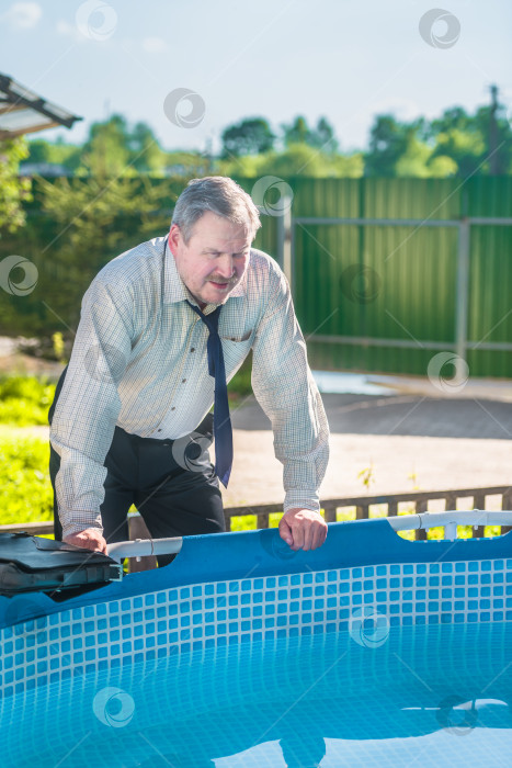 Скачать Мужчина-бизнесмен у бассейна в своем саду после работы в жаркий день. фотосток Ozero