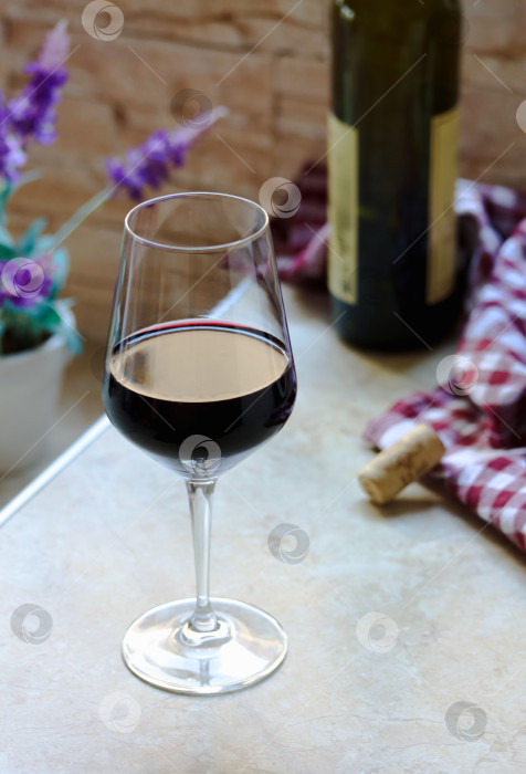 Скачать Бокал вина и бутылка красного вина на домашнем столе, уютная домашняя атмосфера. Бокал красного вина и бутылка вина на кухонном столе, поздний завтрак дома с семьей и друзьями фотосток Ozero