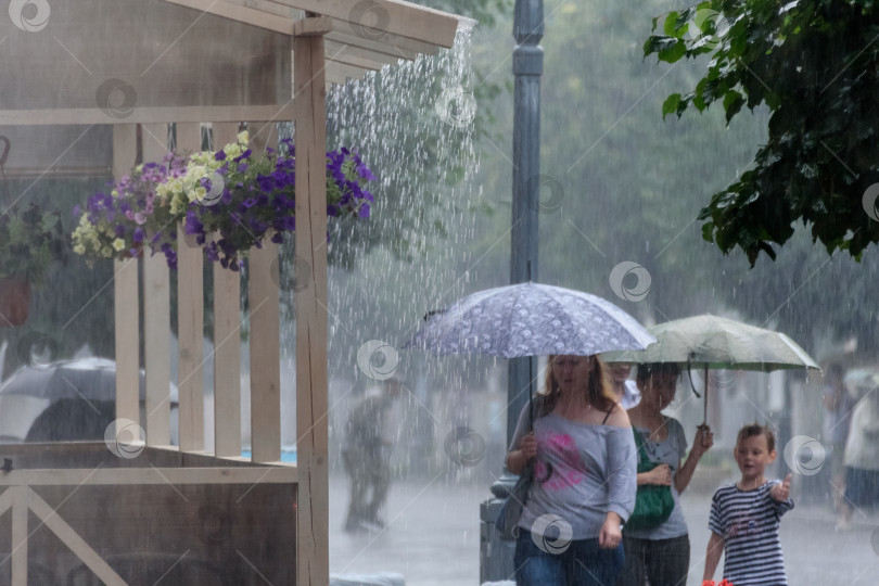 Скачать Россия, Гатчина, июль 2018 года: летний дождь в городе и люди, идущие под дождем мимо кафе фотосток Ozero