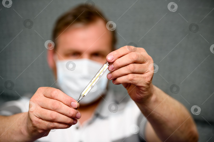 Скачать мужчина в медицинской маске держит в руках термометр - размытый план крупным планом фотосток Ozero