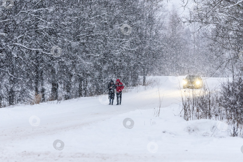 Скачать Снегопад зимой - зимний день, люди идут по дороге м проезжающей машине. Падающий снег на размытом фоне природы фотосток Ozero