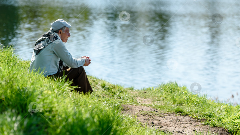 Скачать Пожилой мужчина сидит на берегу озера и отдыхает в одиночестве. Россия. Гатчина. 26 мая 2020 года фотосток Ozero