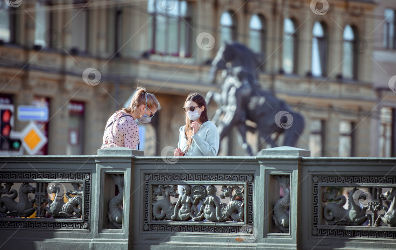 Скачать Россия, Санкт-Петербург, 30 мая 2020 года: две девушки в медицинских масках на прогулке по знаменитому Аничкову мосту в центре города фотосток Ozero