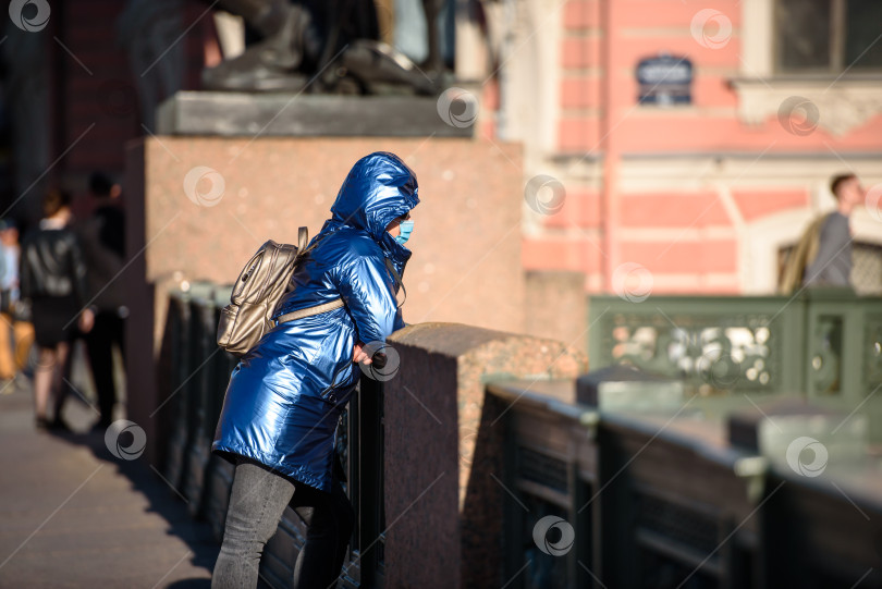 Скачать Россия, Санкт-Петербург, 30 мая 2020 года: туристка в маске в городе, стоя на мосту, смотрит на реку. Аничков мост и река Нева. фотосток Ozero
