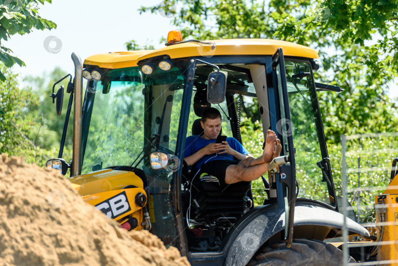 Скачать Россия, Санкт-Петербург, 23 июня 2020 года: водитель трактора отдыхает в кабине во время дорожно-строительных работ в городе фотосток Ozero