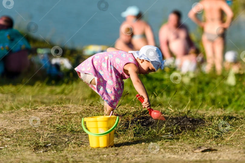 Скачать Россия, Санкт-Петербург, 24 июня 2020 года: маленькая девочка в розовом платье играет в песке на берегу озера фотосток Ozero