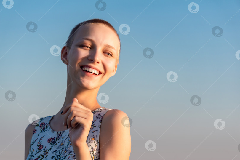 Скачать портрет смеющейся девочки-подростка с короткими волосами в платье на фоне неба фотосток Ozero