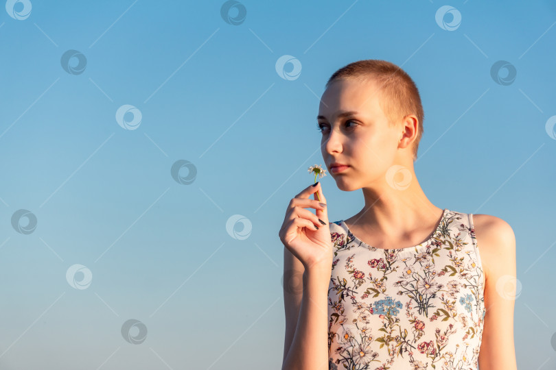 Скачать портрет девочки-подростка с короткой стрижкой в платье, держащей в руке ромашку на фоне неба фотосток Ozero