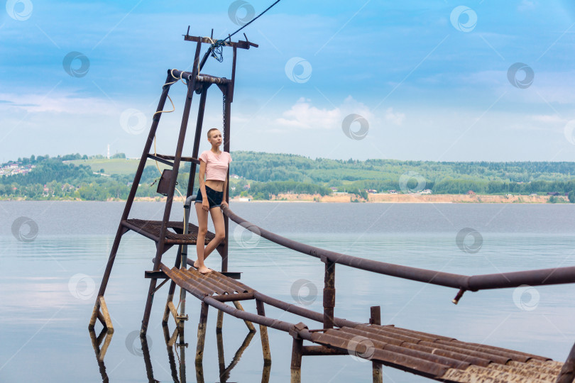 Скачать девушка с короткой стрижкой стоит на деревенском водозаборе на фоне реки в лучах солнца фотосток Ozero