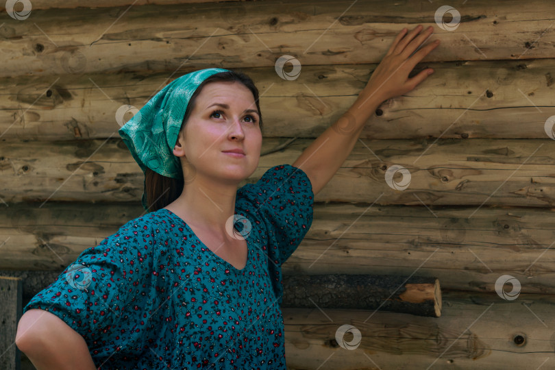 Скачать женщина в традиционном крестьянском платье и головном платке мечтательно смотрит на небо на фоне бревенчатой стены фотосток Ozero