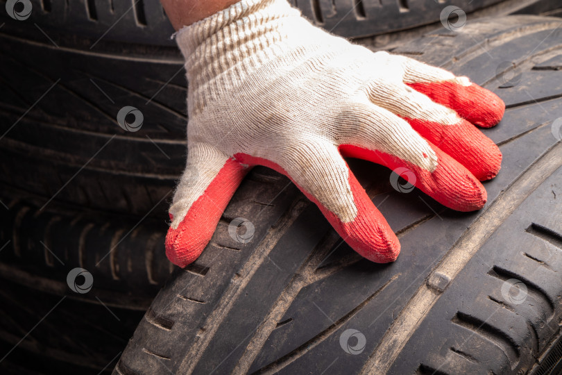 Скачать Рукой в рабочей перчатке прикоснитесь к поверхности старой изношенной шины с индикатором износа. фотосток Ozero
