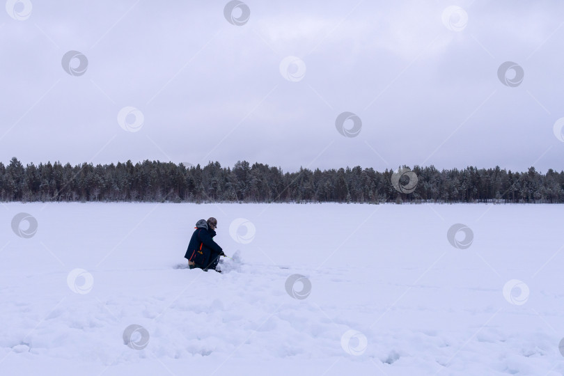 Скачать подледная рыбалка. рыбак ловит рыбу на зимнем озере на фоне леса. фотосток Ozero