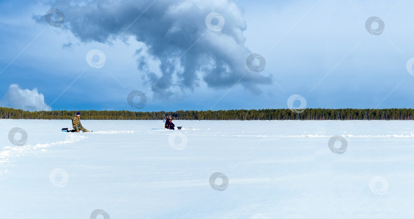 Скачать Подледная рыбалка. рыбаки ловят рыбу на зимнем озере на фоне леса и голубого неба. Пространство для копирования фотосток Ozero