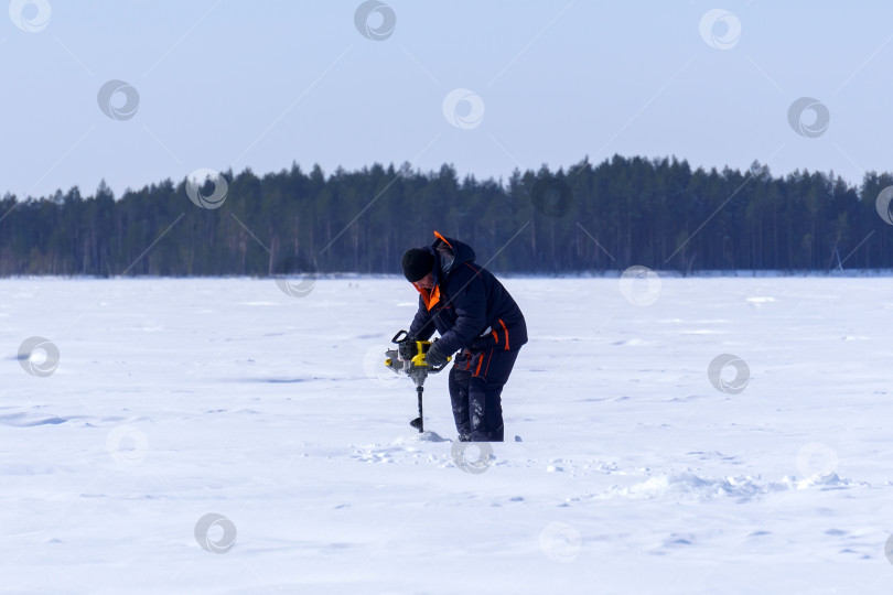 Скачать рыбак на зимнем озере сверлит лед электродрелью фотосток Ozero