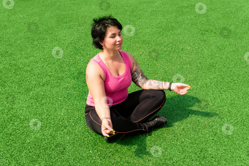 Скачать молодая крепкая пухленькая женщина медитирует на лужайке после тренировки фотосток Ozero