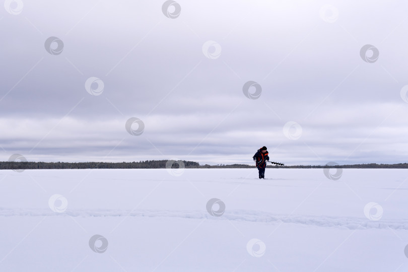 Скачать рыбак на зимнем озере сверлит лед электродрелью фотосток Ozero