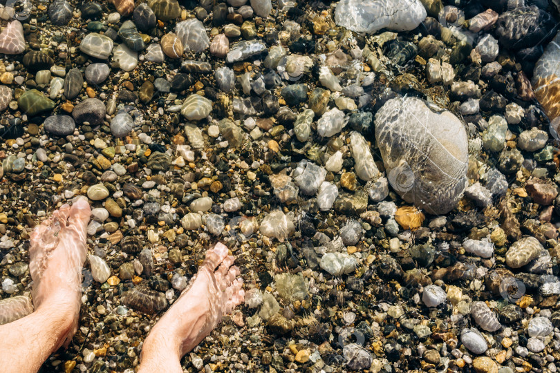 Скачать Морские волны на каменном пляже покрывают скалы и мужские ступни. Концепция летнего отдыха и вакансий. фотосток Ozero