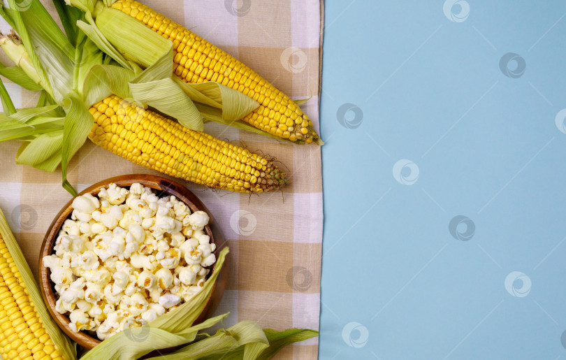 Скачать Вкусный традиционный попкорн и кукурузные початки на синем фоне. Пространство для копирования фотосток Ozero
