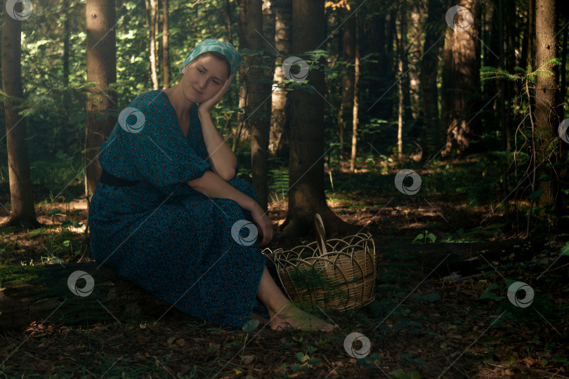 Скачать молодая женщина в народной крестьянской одежде с корзинкой для сбора дикорастущих растений сидит на бревне в хвойном лесу фотосток Ozero