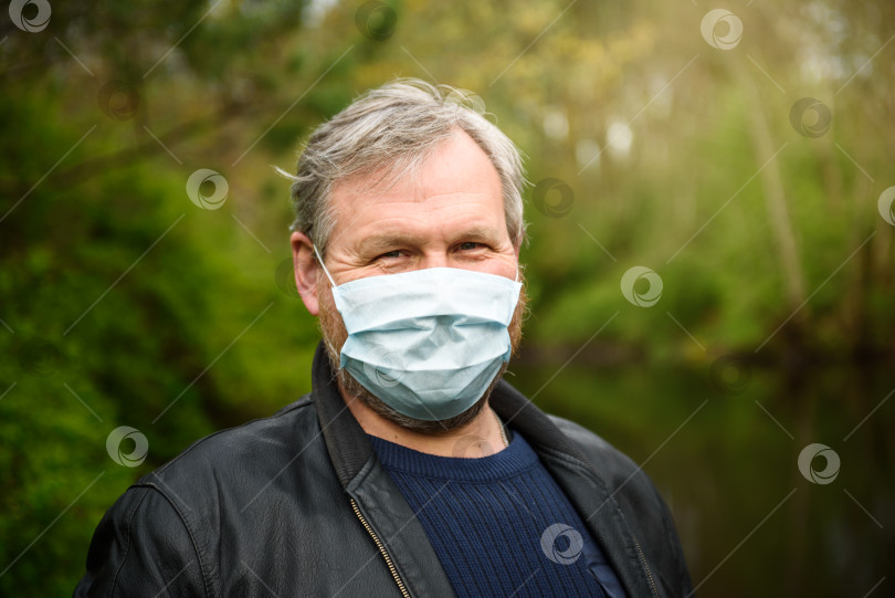 Скачать Счастливый мужчина средних лет в медицинской маске на прогулке на природе. Концепция медицинского обслуживания и карантина. фотосток Ozero