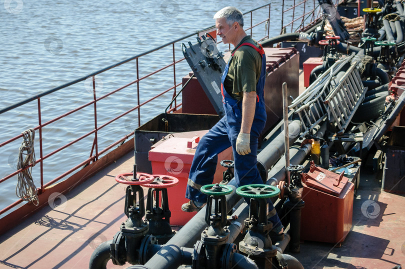 Скачать Россия, Санкт-Петербург, май 2021 года: мужчина в рабочей форме моряка за работой на палубе нефтяного морского танкера фотосток Ozero
