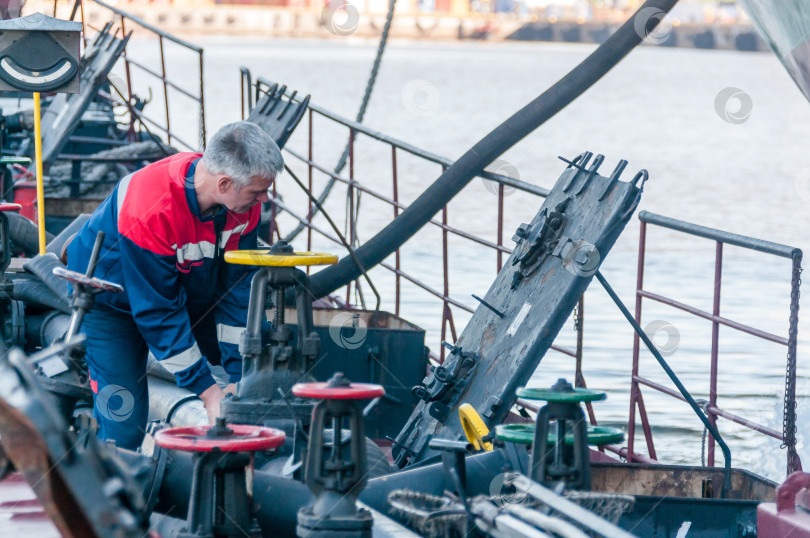 Скачать Россия, Санкт-Петербург, май 2021 года: Рабочий в форме морского пехотинца на палубе нефтяного танкера в бухте в порту фотосток Ozero