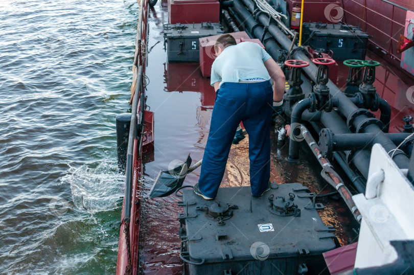 Скачать Россия, Санкт-Петербург, май 2021 года: Рабочий-матрос нефтяного танкера убирает воду с палубы в бухте в порту фотосток Ozero