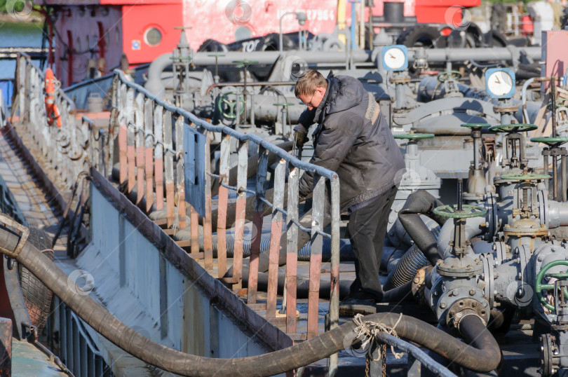 Скачать Россия, Санкт-Петербург, май 2021 года: Рабочий в форме морского пехотинца на палубе нефтяного танкера в бухте в порту фотосток Ozero