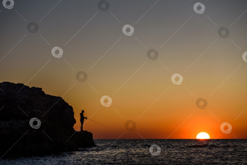 Скачать Море, закат и силуэт рыбака - силуэт мужчины с удочкой на фоне заходящего солнца над морем. фотосток Ozero