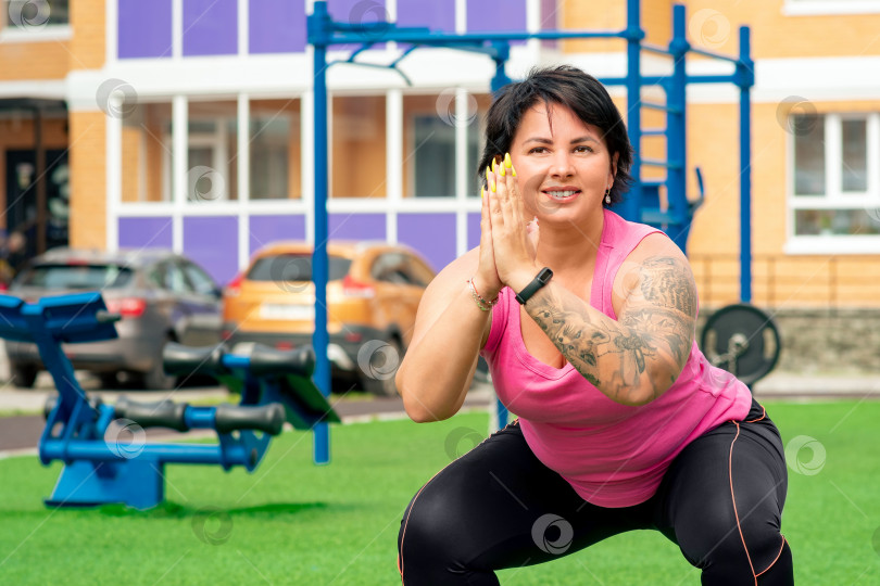 Скачать сильная пухленькая женщина делает приседания на спортивной площадке во дворе городского дома фотосток Ozero