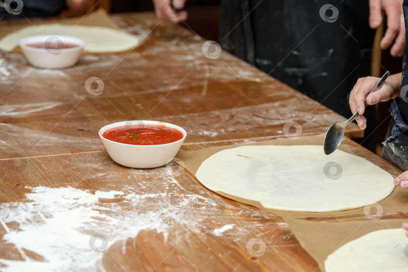 Скачать Крупный план детских рук, готовящих пиццу. Дети выкладывают на основу пиццы овощи и сыр фотосток Ozero