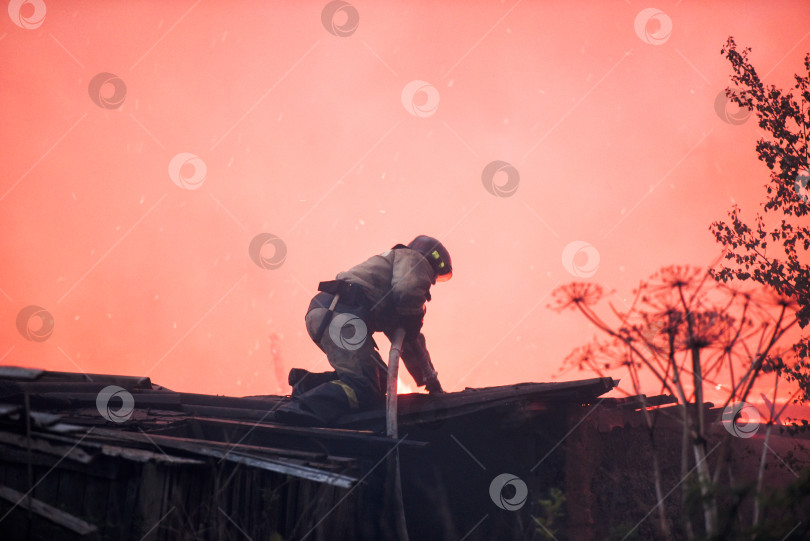 Скачать пожарный тушит огонь на крыше горящего дома фотосток Ozero