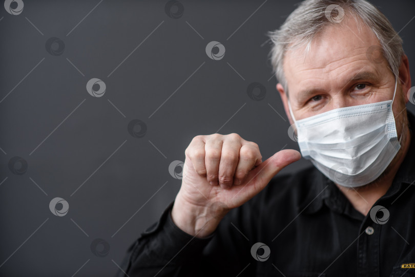 Скачать Счастливый мужчина в стерильной маске для лица, спасающийся от коронавируса covid-19 во время карантинной пандемии, показывает большой палец вверху на темном фоне фотосток Ozero