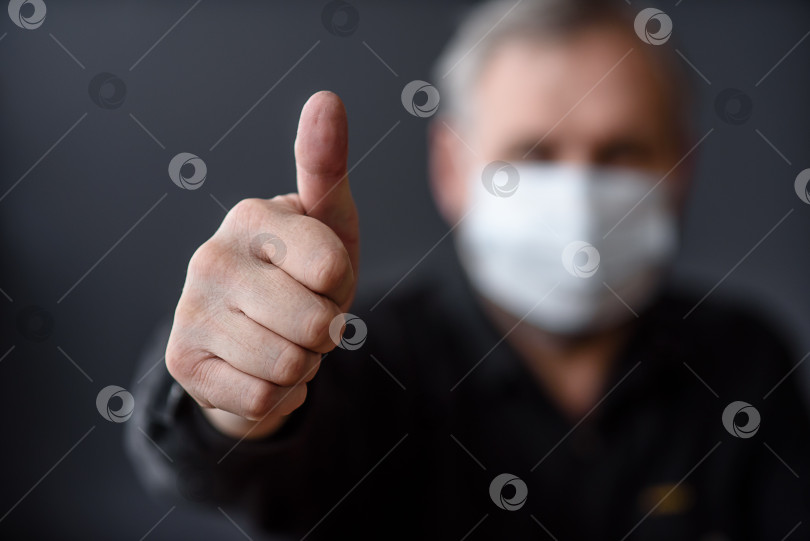 Скачать Человек в маске с поднятым пальцем вверх на темном размытом фоне фотосток Ozero