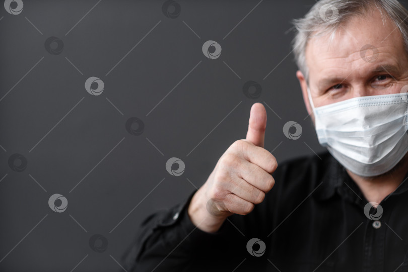 Скачать Счастливый мужчина в медицинской маске показывает большой палец вверх на темном фоне фотосток Ozero