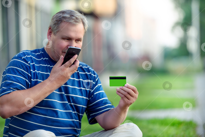 Скачать Мужчина находит на городской лужайке предложения электронной коммерции о покупке онлайн с помощью телефона и кредитной карты фотосток Ozero