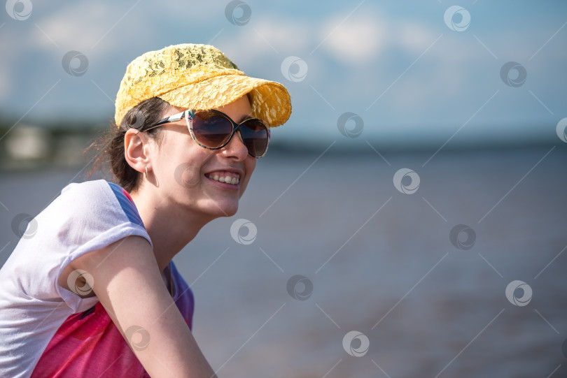 Скачать Счастливая девушка в бейсболке и солнцезащитных очках улыбается на фоне морского пляжа фотосток Ozero