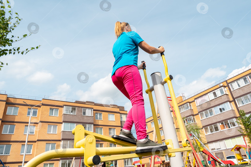 Скачать молодая женщина занимается на уличном тренажере эллиптический кросс тренажер в городском дворе фотосток Ozero