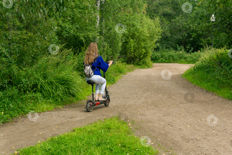 Скачать молодая женщина едет на электрическом скутере по дорожке в парке фотосток Ozero