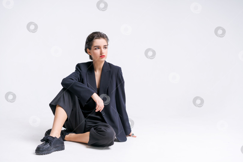Скачать Красивая молодая бизнесвумен в модном черном костюме позирует, сидя на полу фотосток Ozero