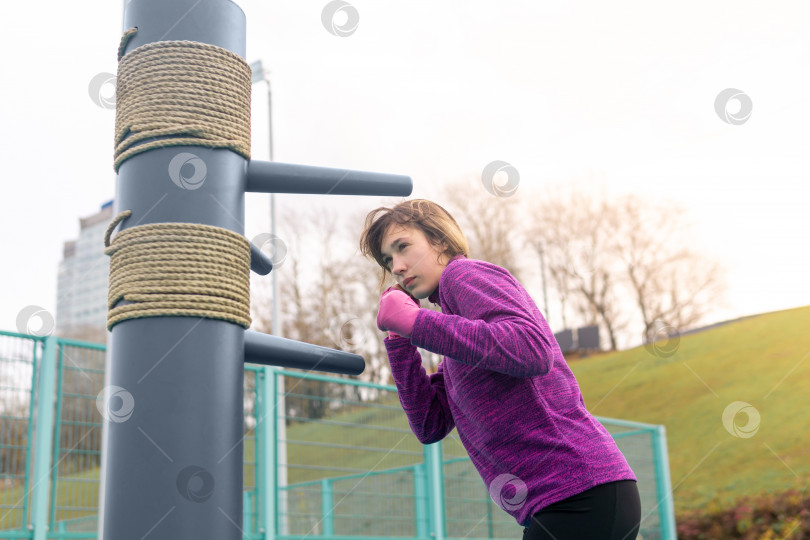Скачать молодая женщина, практикующая боевые искусства в одиночку на спортивной площадке с традиционными манекенами фотосток Ozero