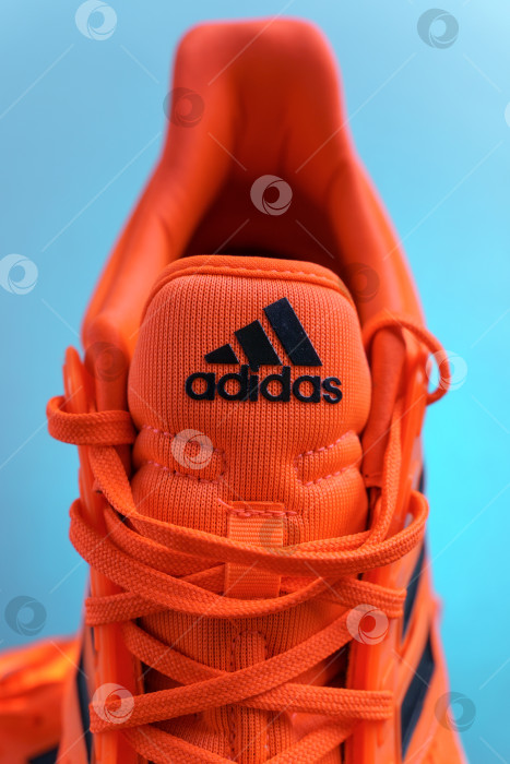 Скачать Тюмень, Россия - 13 ноября 2021 года: Оранжевые кроссовки adidas на синем фоне. Вертикальная фотография фотосток Ozero