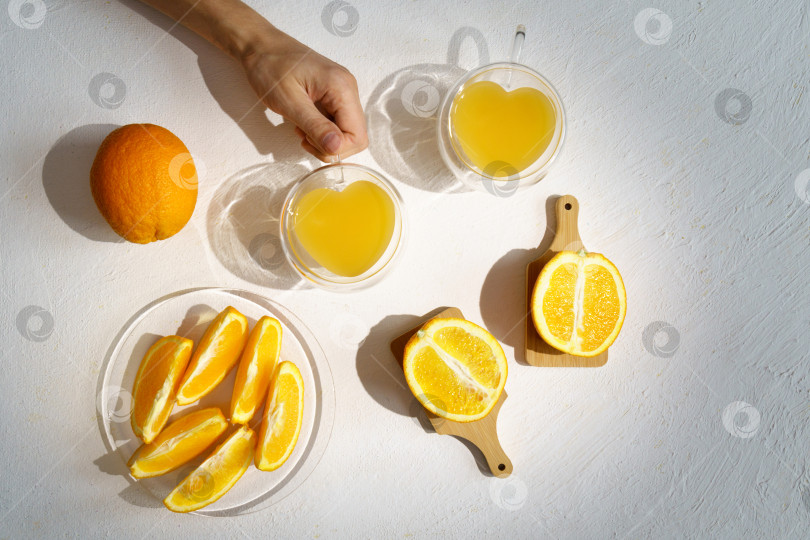 Скачать Свежевыжатый апельсиновый сок в стакане с листьями, нарезанными апельсинами и льдом на белом фоне. Вид сверху фотосток Ozero