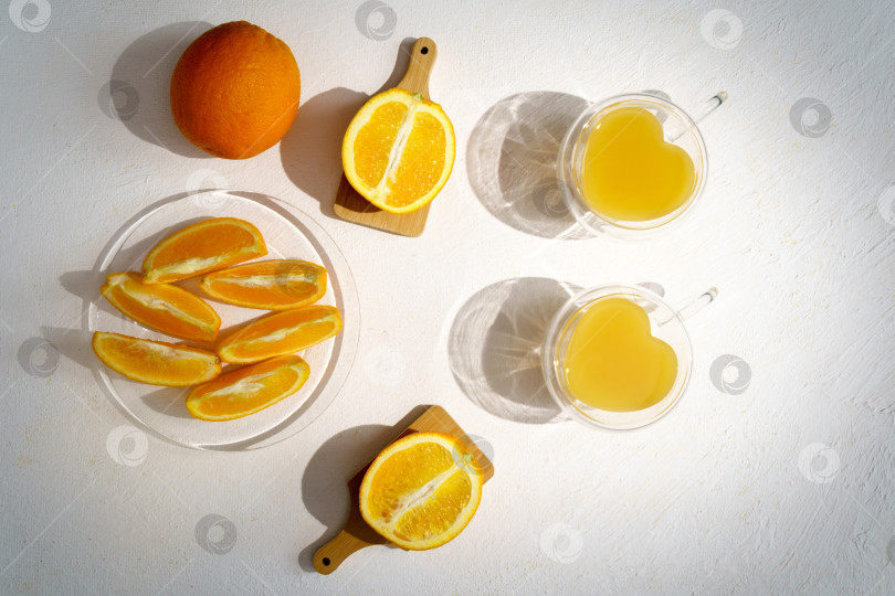 Скачать Свежевыжатый апельсиновый сок в стакане с листьями, нарезанными апельсинами и льдом на белом фоне. Вид сверху фотосток Ozero