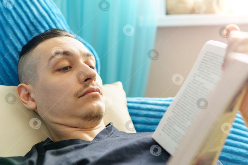Скачать Концепция досуга, образования, литературы и дома крупным планом изображен мужчина, лежащий дома на диване и читающий книгу фотосток Ozero