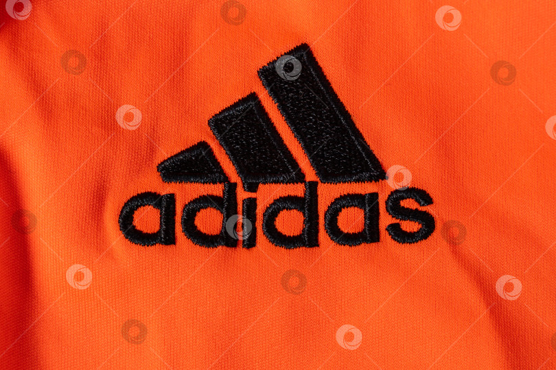 Скачать Тюмень, Россия - 11 мая 2022 года: логотип Adidas крупным планом на оранжевом фоне. Adidas - немецкая транснациональная корпорация по производству одежды и обуви фотосток Ozero